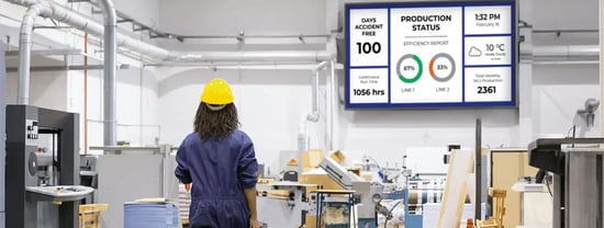 A worker in a factory setting monitors machinery with production data displayed on screens