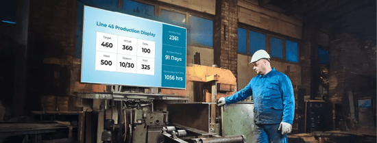 A worker in a manufacturing unit with digital signage displaying production data in the background