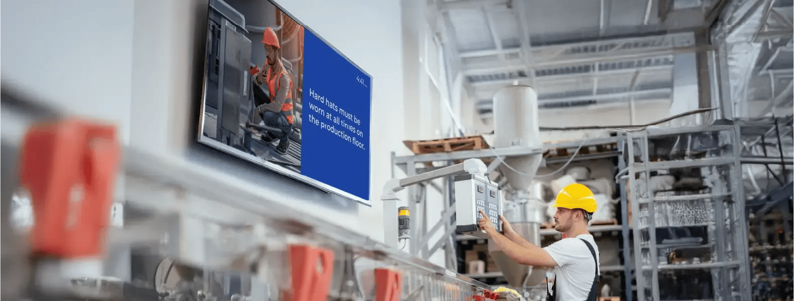 A factory worker reviewing tasks with production metrics displayed on a screen.