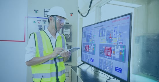 actory workers viewing a digital signage screen showing a real-time alert for a machine downtime.